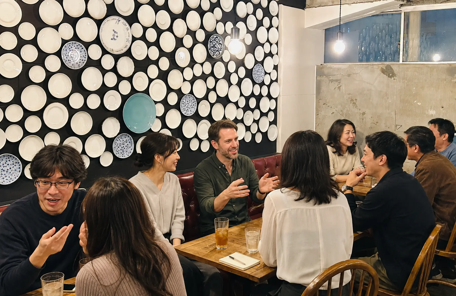 多くの大人が複数のテーブルに分かれて英語を話す英会話カフェ会場